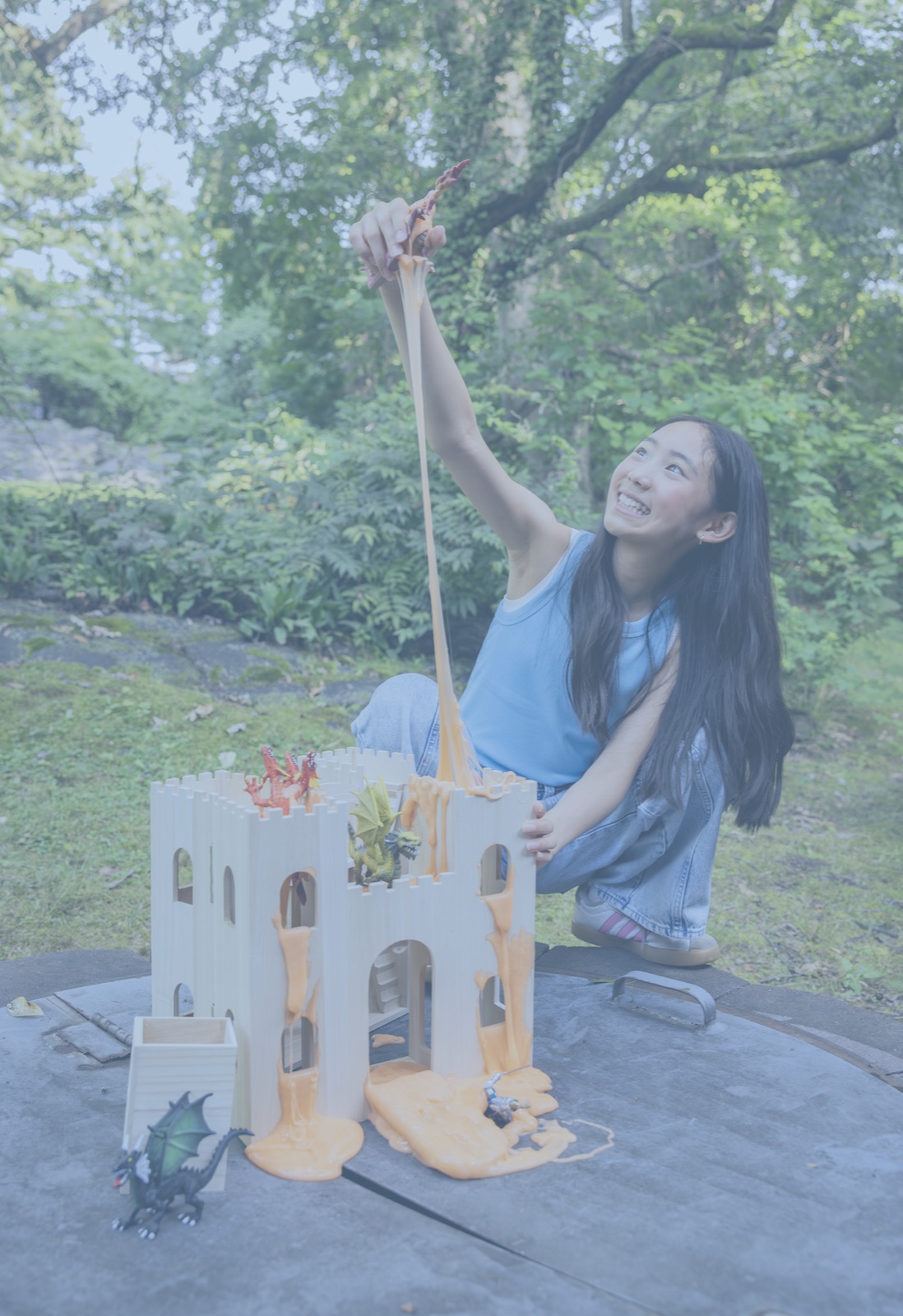 Girl pouring orange Elmer's slime down a castle playset with toy dragons outdoors