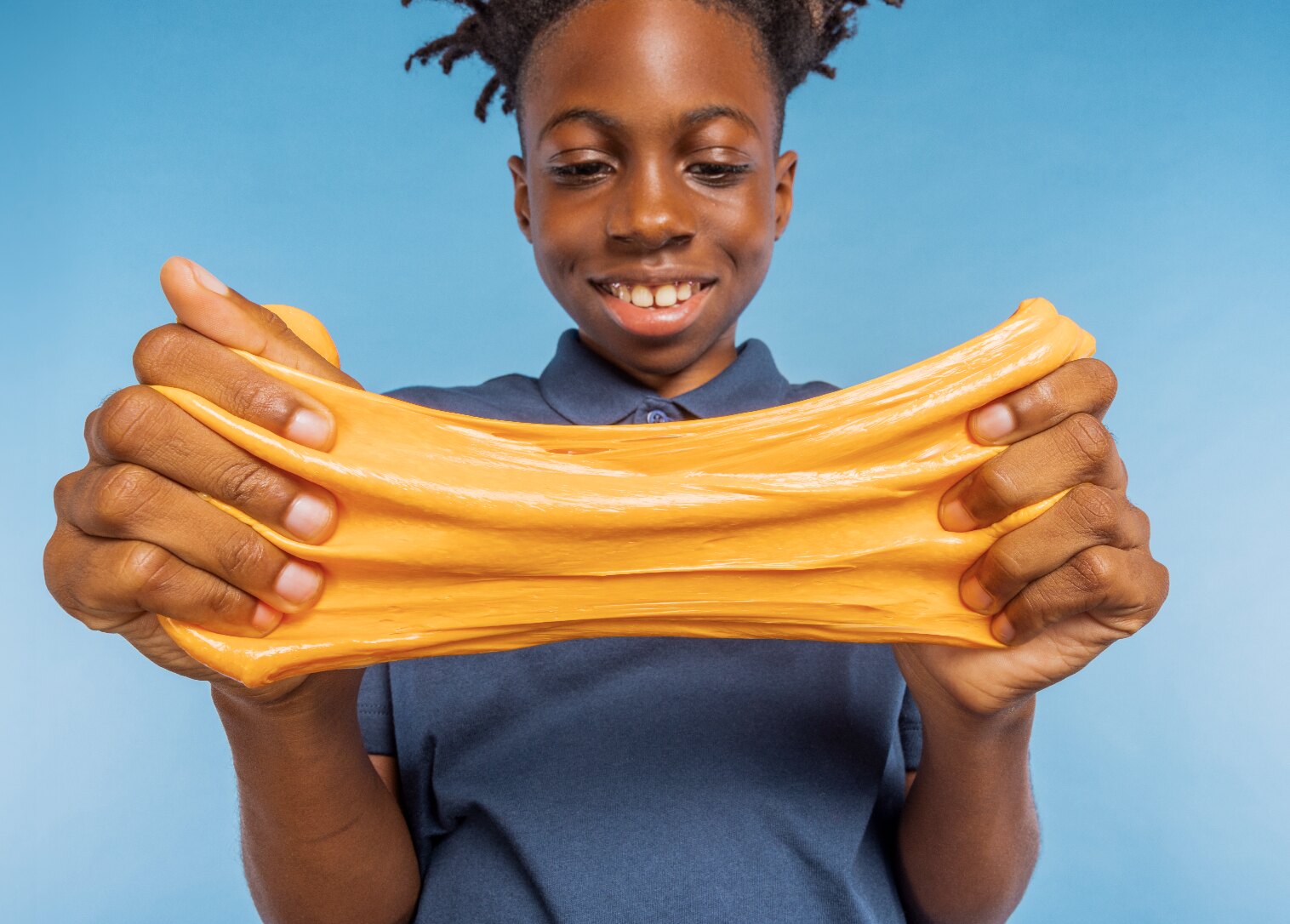 Boy stretching orange Fruity Elmer's slime on a blue background