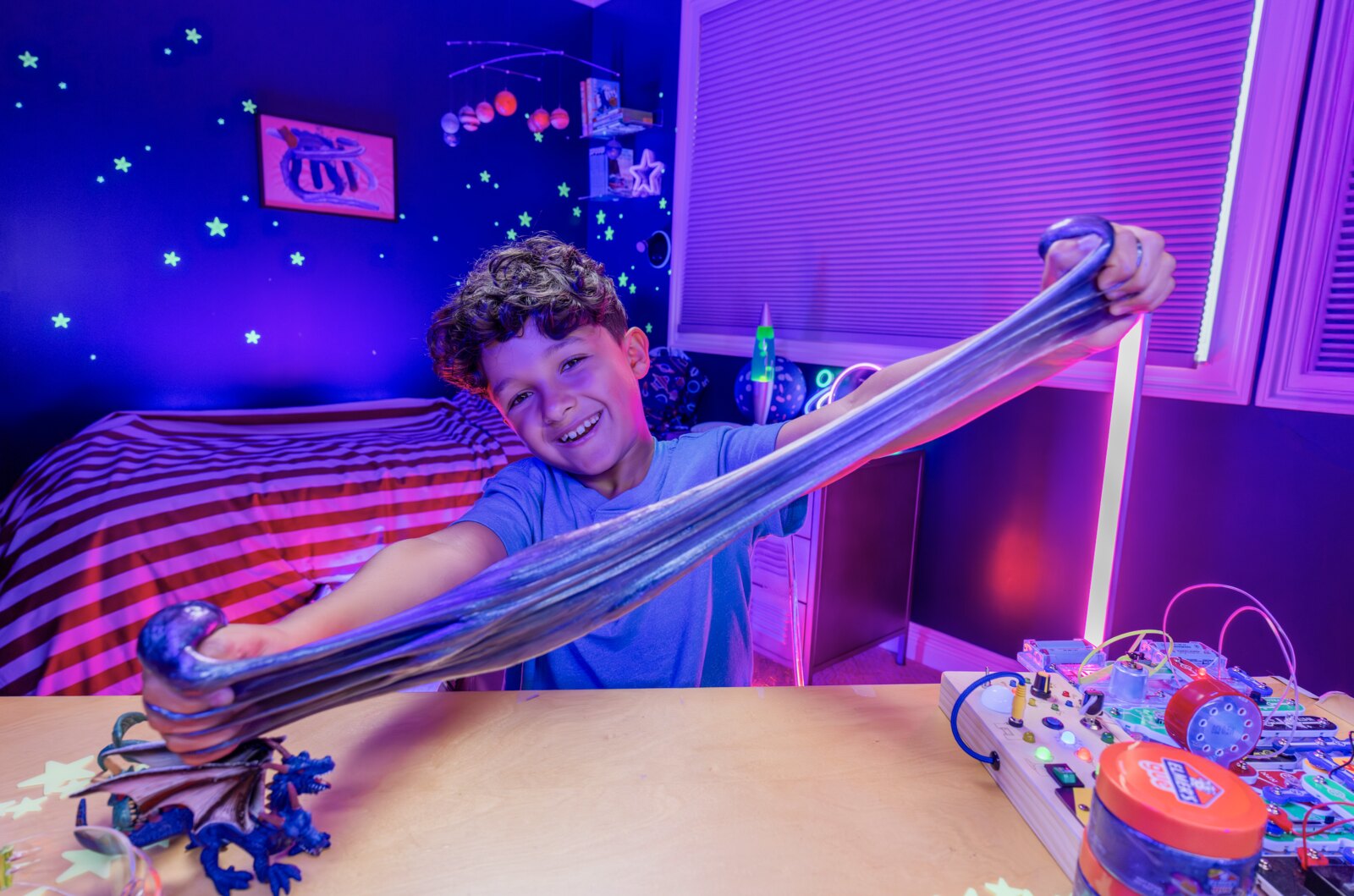 Boy in a starry-night room playing with Galaxy Elmer's slime