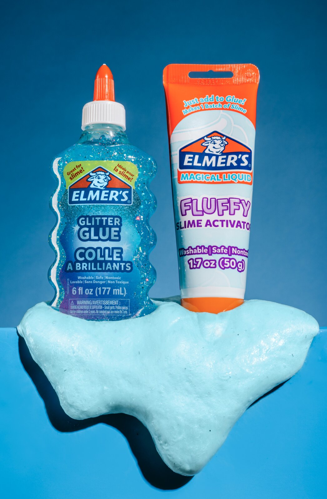 Elmer's Glitter Glue bottle and Fluffy Activator tube with a slime cloud on a blue background