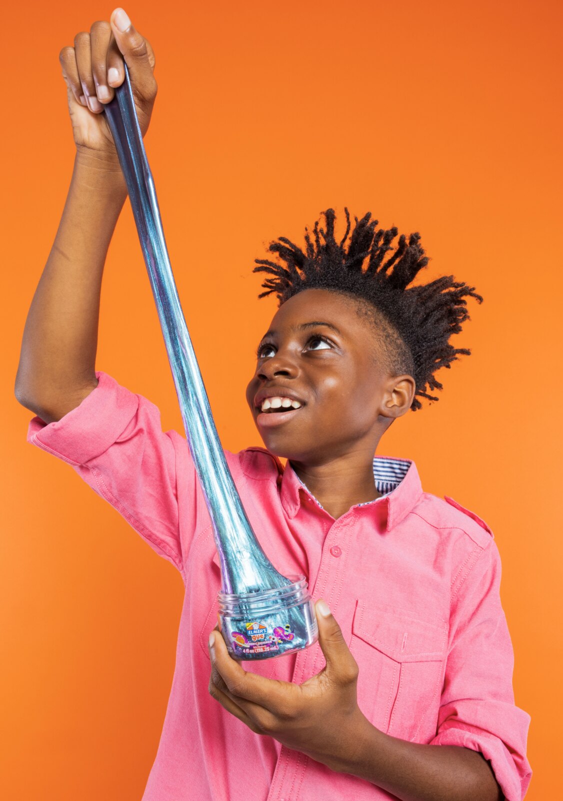 Boy in a pink shirt stretching Glitter Elmer's slime upward on an orange background