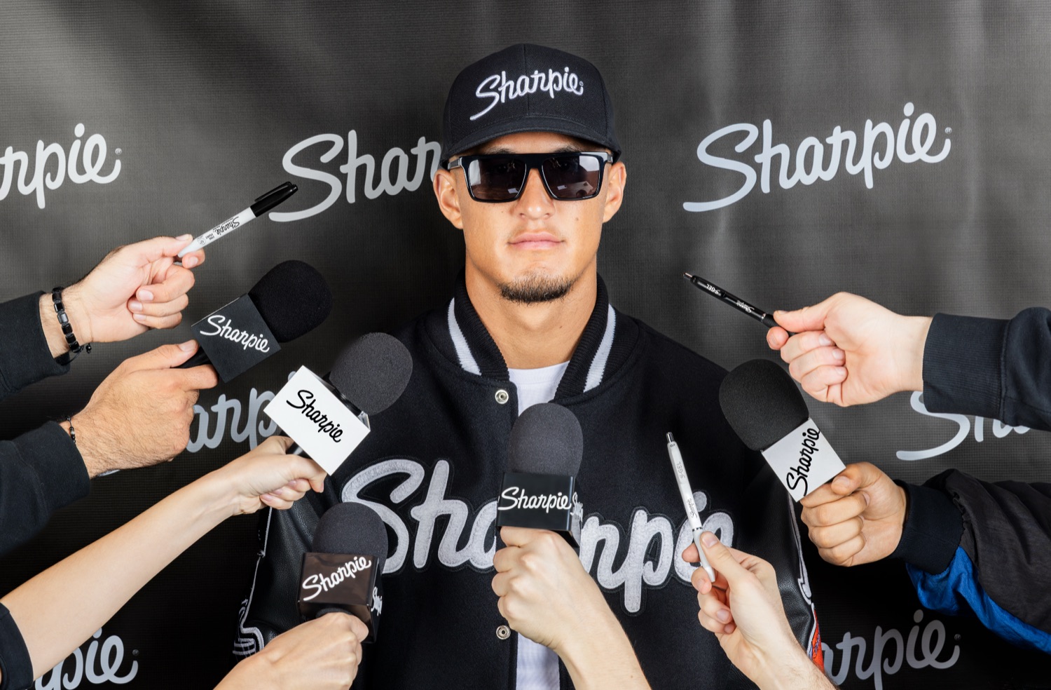 Athlete in Sharpie cap and varsity jacket surrounded by Sharpie-branded microphones and pens