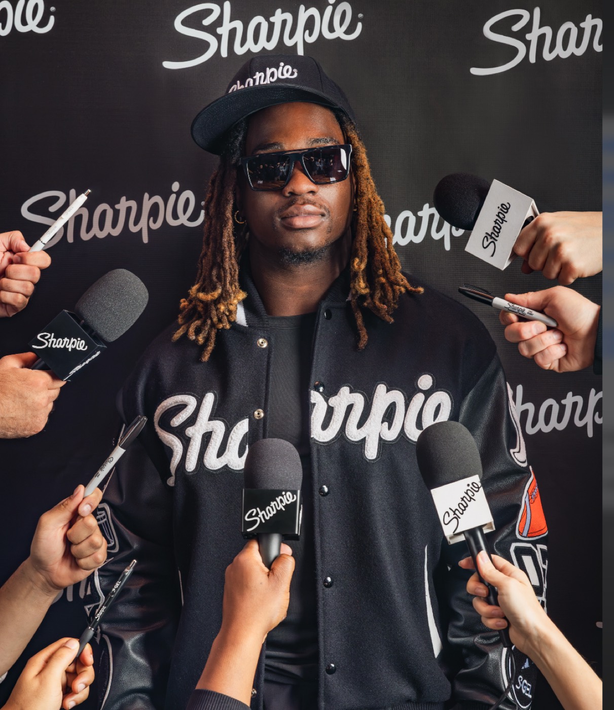 Athlete in a Sharpie varsity jacket facing a press scrum of Sharpie-branded microphones